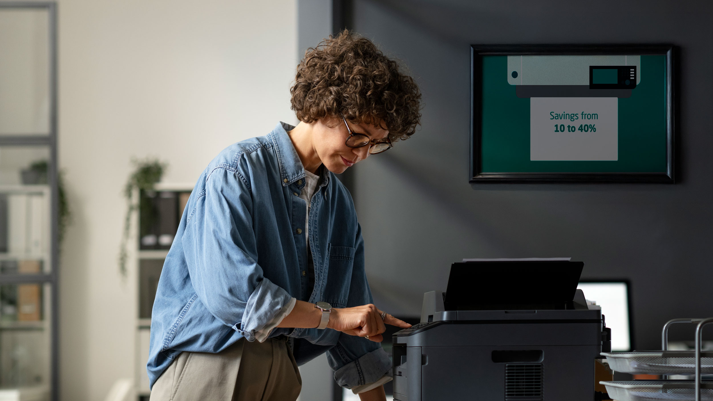 Woman in office stands pressing a button on a black printer she has curly hair